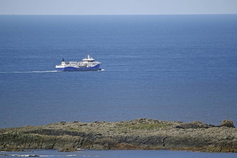 A large fishing vessel navigates the blue sea along the rocky coastline, Sumburgh Head, Shetland