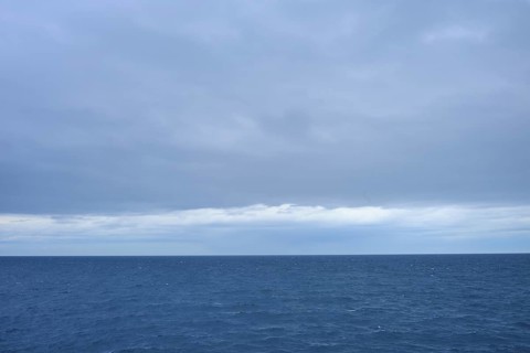 A calm sea stretches to the horizon with thick clouds in the sky, summer, Cook Strait, North