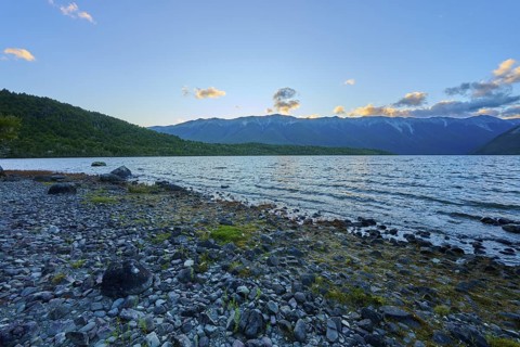 Rocky beach at dusk, calm lake with mountains in the background, summer, Lake Rotoiti, Saint