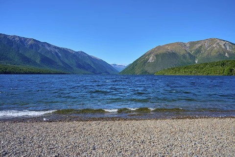 Wide view over a pebble beach to a lake surrounded by mountains, summer, Lake Rotoiti, Saint