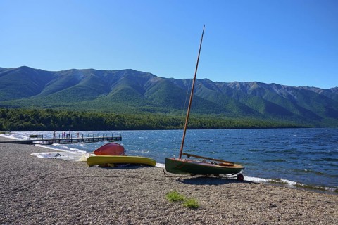 Boats moored on the shore of a lake with a breathtaking mountain backdrop and clear blue sky,
