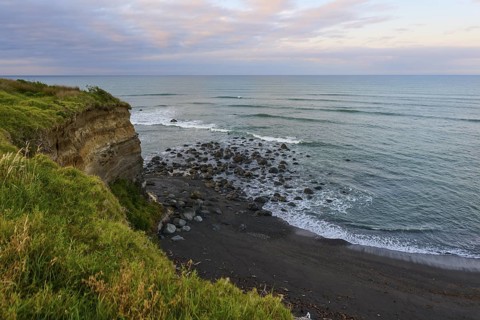 Seaside cliff with rocks and green vegetation under a cloudy sky, summer, Opunake, Taranaki, North