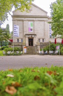 Historic building with signs and stairs, surrounded by trees and outdoor garden furniture, Baden