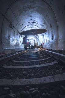 A mysterious tunnel with rails and graffiti, illuminated by a diffuse light. A figure stands under