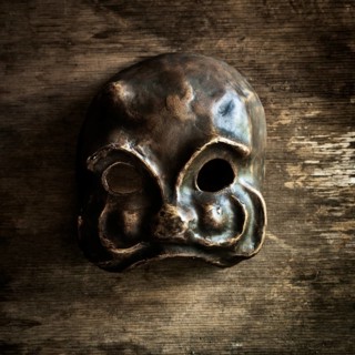 A handcrafted skull mask rests on a weathered wooden surface, highlighting its unique shape and