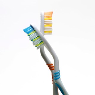 The image features two toothbrushes twisted together, highlighting their vibrant bristle colors and