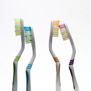 Four vibrant toothbrushes in varied colors stand side by side against a simple background,