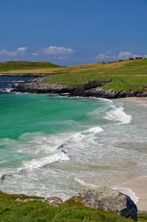 Picturesque coastal landscape with green water and waves meeting the sandy beach under a blue sky,