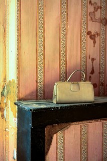 A lonely handbag sits on a worn shelf in an abandoned house, surrounded by peeling wallpaper. The