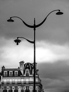 An ornate street lamp rises high against a backdrop of a moody, cloud-filled sky, highlighting the