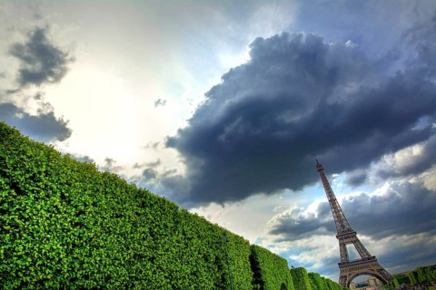 Clouds blanket the sky above the Eiffel Tower, creating a striking contrast with the greenery below