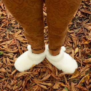 A young woman stands among fallen leaves, wearing warm, fluffy shoes that provide comfort. The