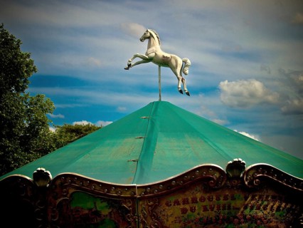Paris. A carousel topped with a striking white horse in mid-leap stands under a vivid green canopy
