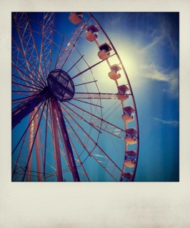 Visitors admire the towering Ferris wheel as it stands against a vibrant blue sky. The sunlight