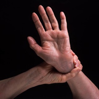 Two hands are featured in contrasting positions, highlighting the skin's texture and the grace of