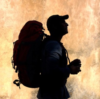 A silhouette of a walker stands against a vibrant, textured backdrop, holding supplies in hand,