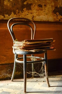 An old wooden chair is prominently positioned with a pile of yellowed newspapers resting on the