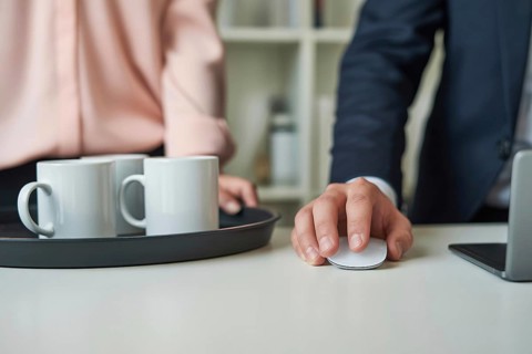 Close up of a woman's hand in pastel pink blouse holding a tray with white coffee mugs next to a