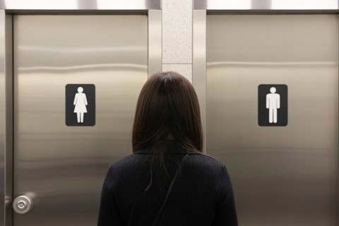 Woman in front of men's and women's bathroom doors. Concept of public restroom access and trans