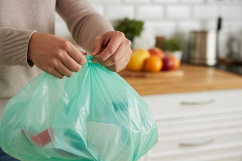 Woman tying up a garbage bag in a home kitchen as part of daily waste disposal. Generative ai, AI
