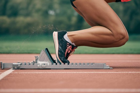 Close-up of female athlete in running shoes on starting block at running track. Concept of speed