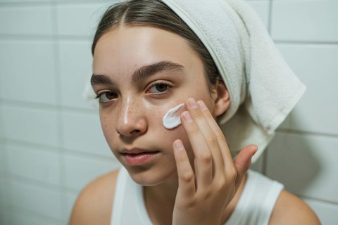 Teenage girl applying skin cream in bathroom. Honest daily skincare and self-care routine.
