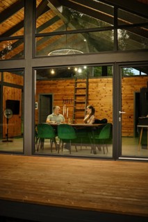 A modern wooden cabin, viewed from outside in the evening. Through large glass windows and doors a