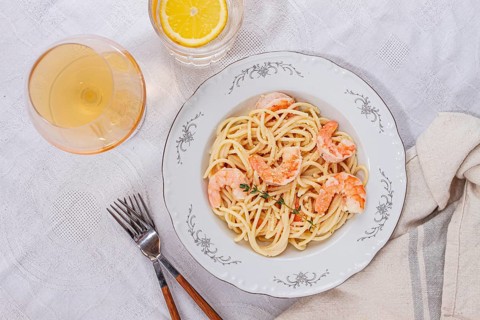 Pasta with shrimp and thyme, served on a white plate, with a glass of white wine, the table is set,