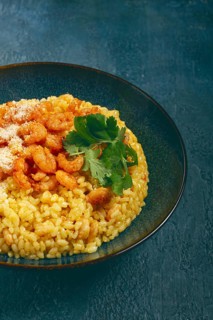 Risotto with shrimp, in a bowl, on a textured surface, with a side dish of fresh coriander,