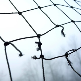 A close-up view of worn netting with frayed edges, suspended in a misty landscape. The atmosphere