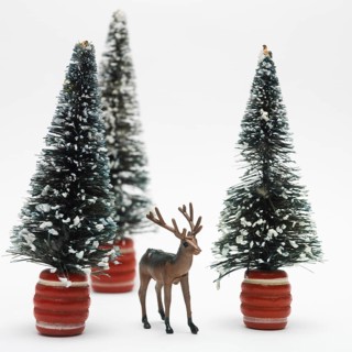 A detailed deer figurine stands in front of two snowy miniature trees, creating a festive