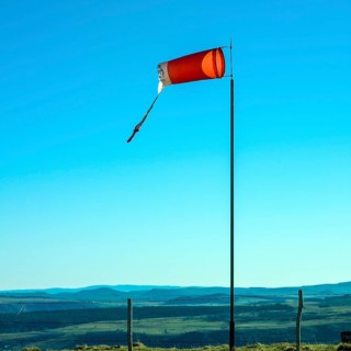 A windsock stands prominently on a pole in Auvergne, gently blowing in the breeze. The clear blue