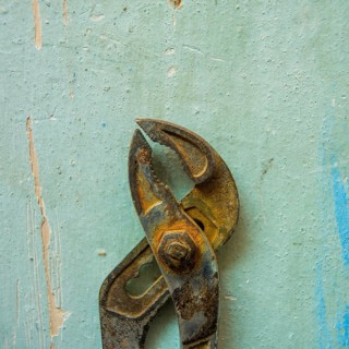 A pair of rusty pliers hangs on a worn blue wall, showcasing the wear and tear of years in a
