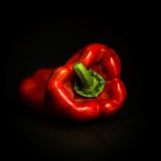 The vibrant red bell pepper, with its glossy skin, is positioned on a rich black background,