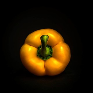 A bright yellow bell pepper showcases its glossy skin with a green stem, beautifully contrasting