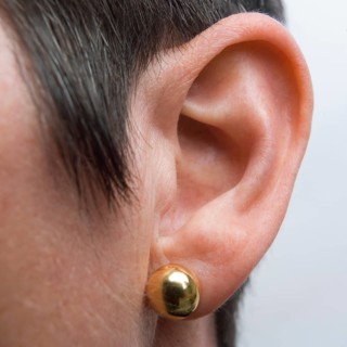 Detailed view of a woman's ear featuring a shiny drop earring. The focus is on the ear structure