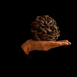 A hand supports a uniquely crafted ball made of intertwined materials, resting against a dark