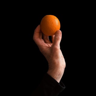 A hand gracefully holds a bright orange, emphasizing its round shape and textured skin. The dark