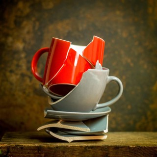 Stack of broken red mug and gray plate pieces on rustic wooden surface, showcasing fractured