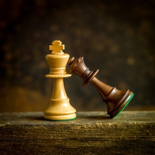 Two intricately designed chess pieces, a golden king and a dark queen, lean against each other on
