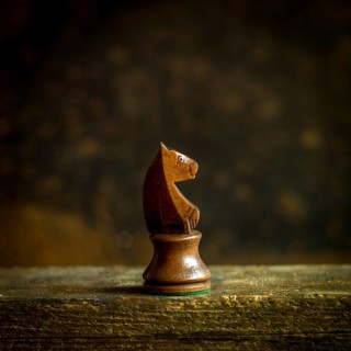 A beautifully crafted wooden chess knight piece stands prominently on a wooden surface. The