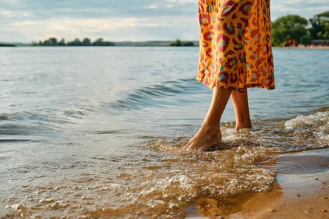 Woman wading in shallow water wearing bright dress by the lakeside during golden hour
