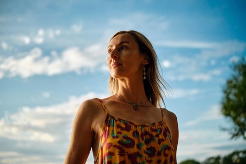 A woman stands outdoors, wearing a vibrant, colourful dress. She gazes into the distance as the sun