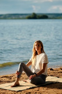A woman sits peacefully on a mat by the lake, enjoying the serene atmosphere as the sun sets. She
