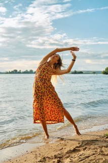 A woman dressed in a vibrant, patterned dress dances gracefully near the edge of a lake. The sun