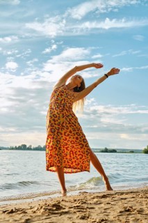 A joyful woman stretches gracefully on the sandy shore as the sun sets over the water. The vibrant