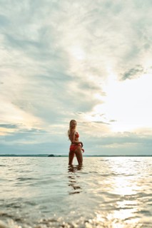 A woman stands in shallow water, enjoying the tranquil surroundings as the sun sets on the horizon.