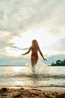 A young woman in a red swimsuit joyfully runs into the lake, creating splashes as she embraces the