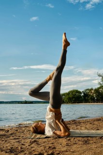 A dedicated individual performs a yoga pose on a sandy beach by the tranquil lake. The sun shines