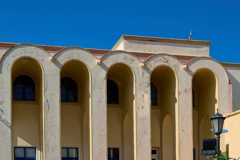 Primary school, Beige-coloured building with large arches against a clear blue sky, Armando